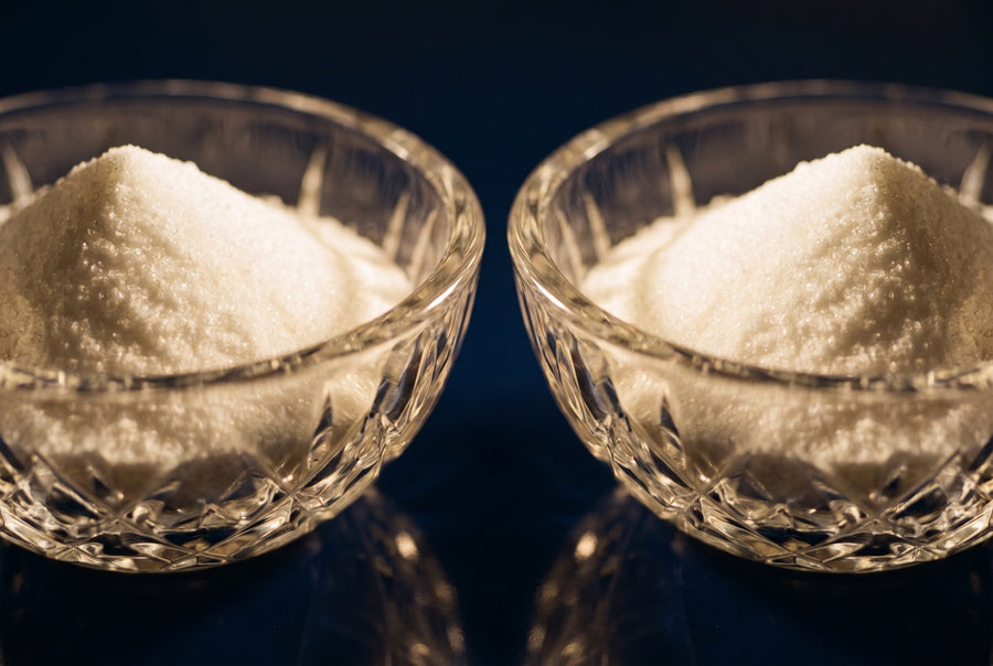 Two matching cut-crystal bowls of white crystalline powder side by side on a dark navy surface