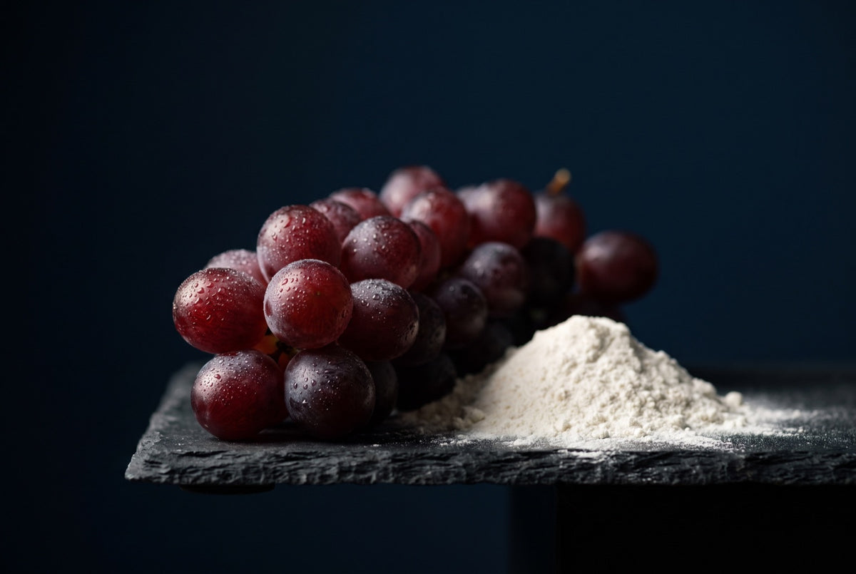 A bunch of red grapes with dewdrops beside a mound of white powder on a slate ledge