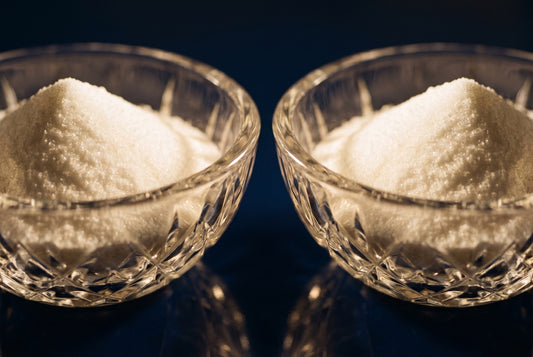 Two matching cut-crystal bowls of white crystalline powder side by side on a dark navy surface