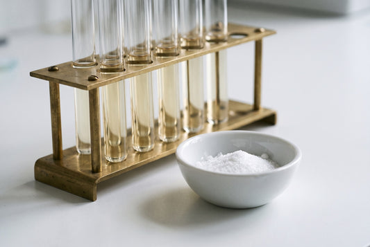 Test tubes of pale straw-coloured liquid in a brass rack beside a dish of white crystalline powder