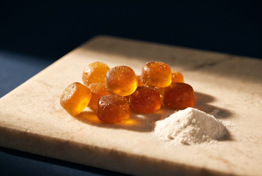 Amber gummies beside a small heap of white powder on a cream marble slab