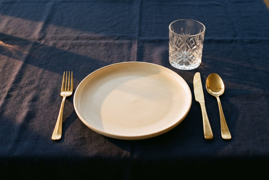 An empty plate with gold cutlery and a crystal glass on a navy tablecloth