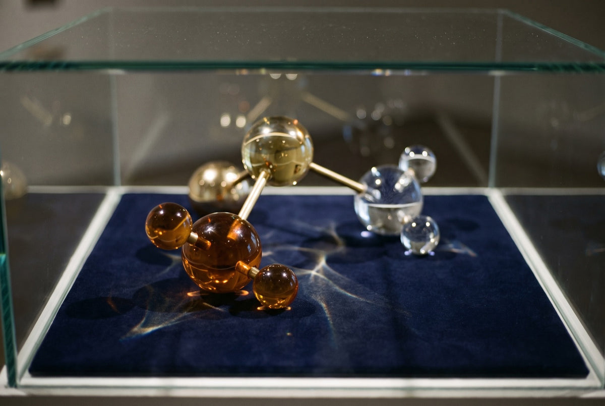 A glass-and-brass molecular model on navy velvet inside a glass display case