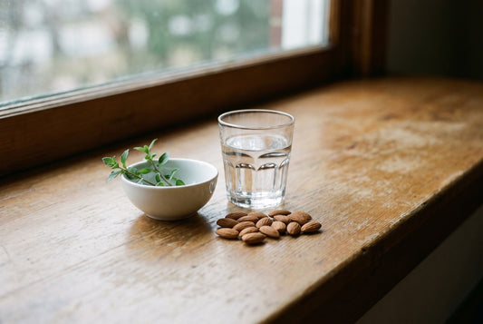 A glass of water, a small bowl of greens and a handful of almonds on a sunlit window ledge