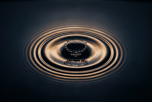 A single drop striking dark water and sending out golden ripple rings