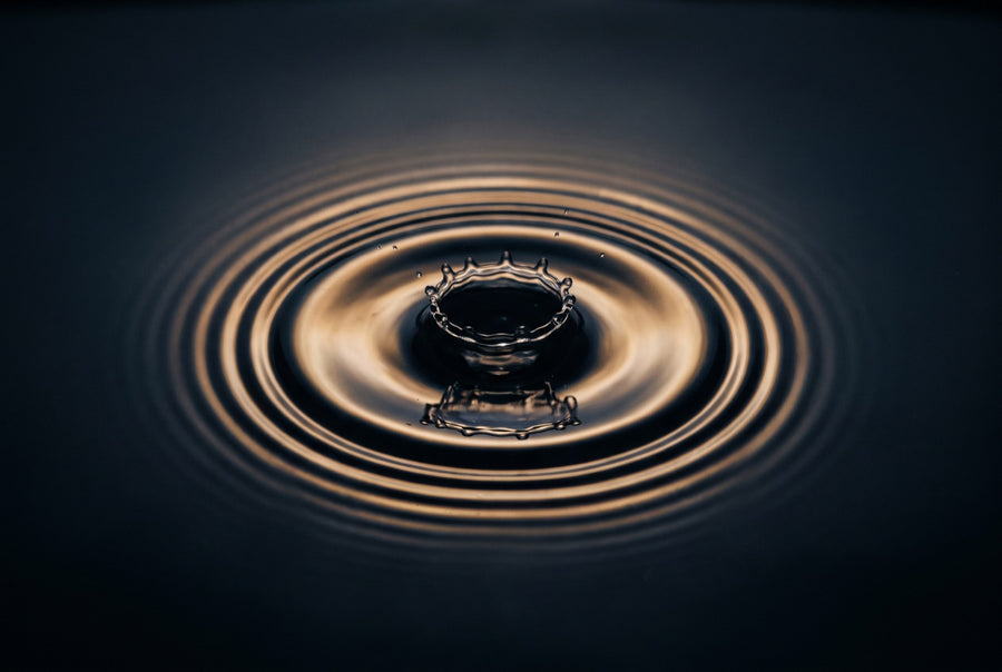 A single drop striking dark water and sending out golden ripple rings