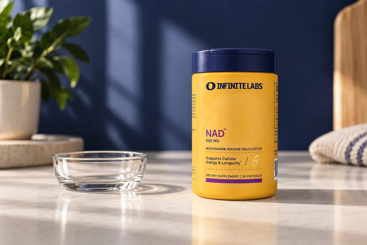 InfiniteLabs NAD+ bottle beside an empty clear dish on a pale counter.
