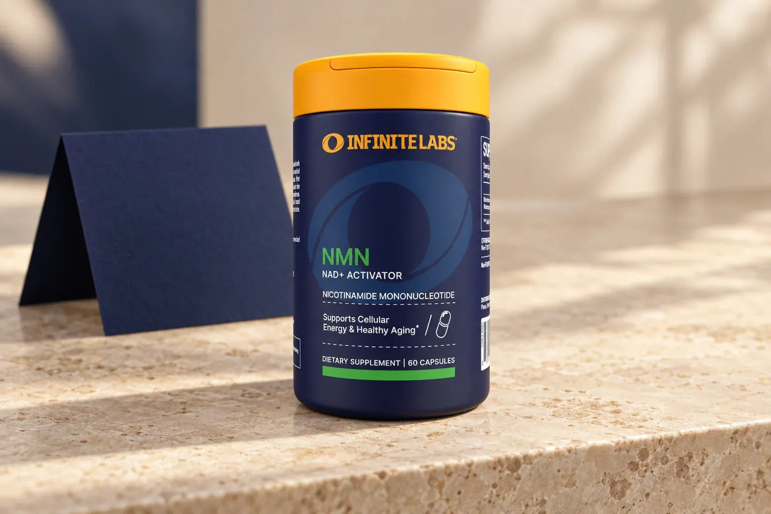 Upright InfiniteLabs NMN bottle beside a folded navy card on pale stone.